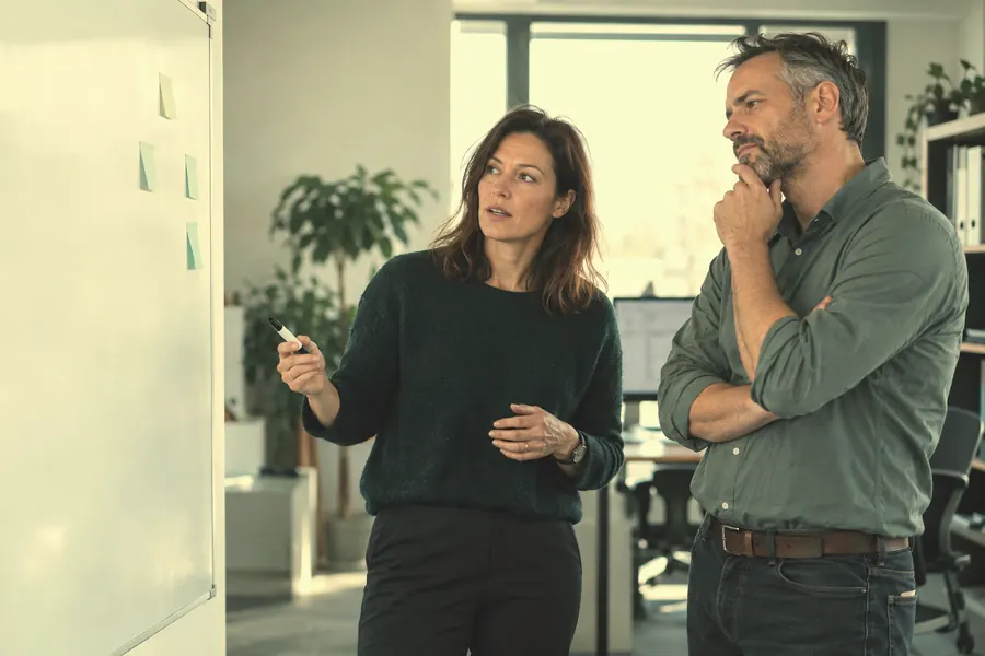 A talent acquisition lead and a hiring manager discuss a role at a whiteboard.